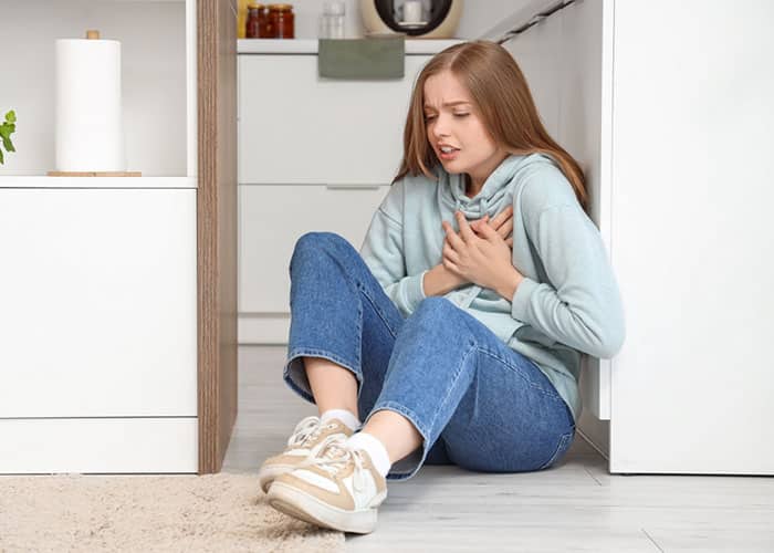 Young woman sitting on the floor experiencing a panic attack with chest pain and distress, highlighting the importance of professional mental health services and anxiety treatment support.