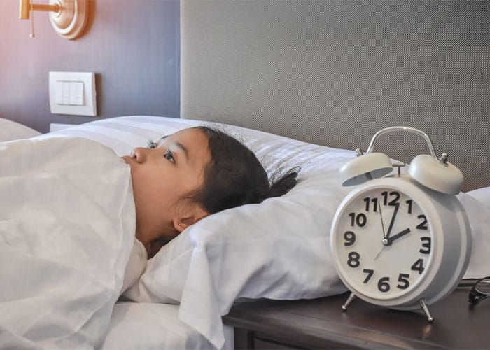 Young woman lying awake in bed at night next to an alarm clock, illustrating sleep disorders and the need for consultation with a psychiatrists doctor in Lahore for proper diagnosis and treatment.