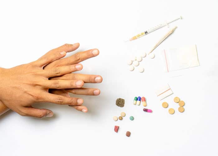 Hands next to drugs, pills, syringe, and substance items representing drug addiction treatment by a top psychiatrist in Lahore